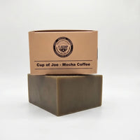 Top view of Flagship Soap Company "Cup of Joe" Mocha Coffee soap bar. The tan packaging prominently displays the mocha coffee scent and the circular "Shit-Shower-Lather" seal. This exfoliating coffee soap is a premium veteran-owned grooming product for men.
