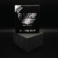 Front-facing shot of the Vendetta soap box by Flagship Soap Company. The corner label identifies the sweet vanilla and cedarwood scent. The box sits atop a rugged, deep-grey activated charcoal soap block.