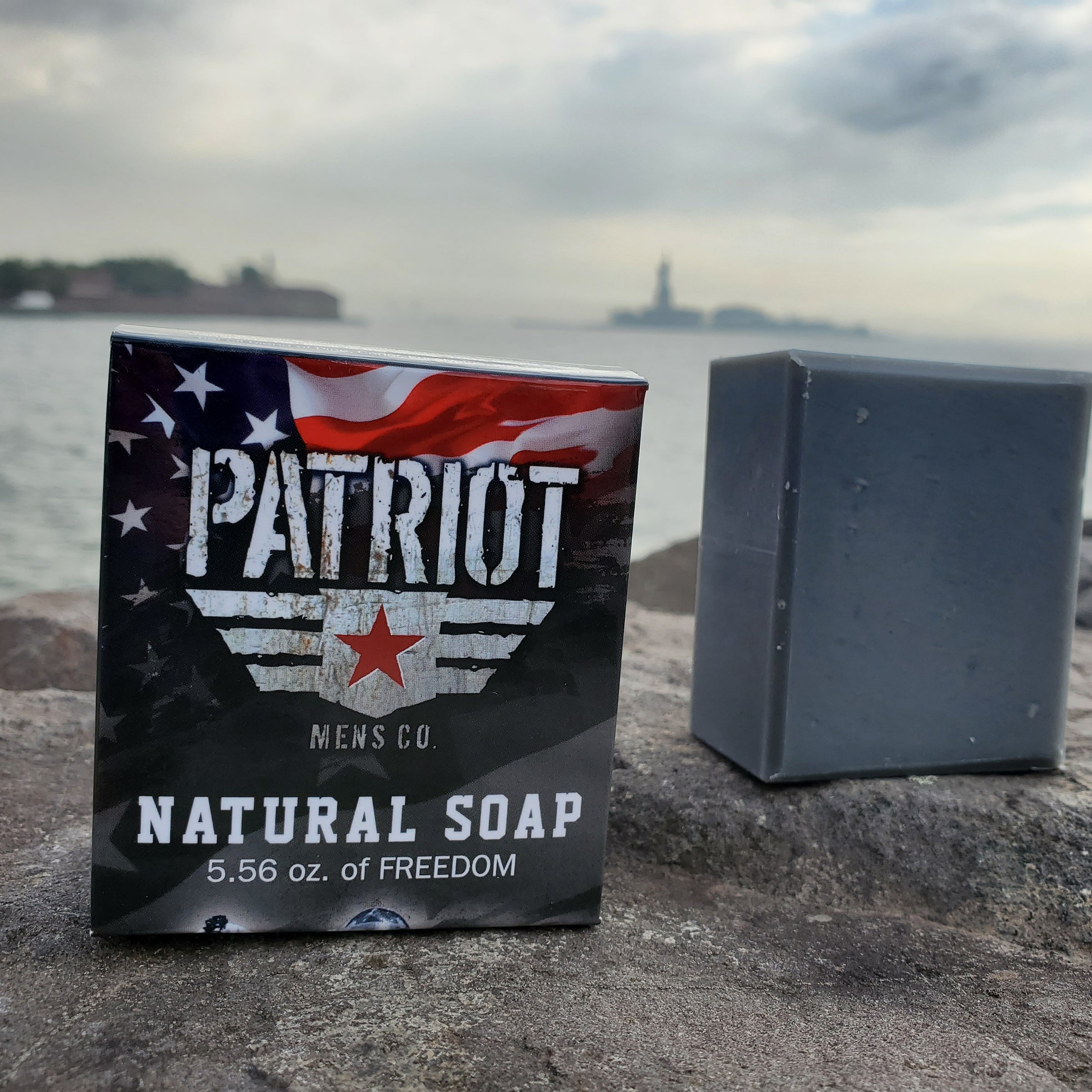 Down Range natural men's soap, smell's like gunpowder, by Patriot and Company activated charcoal soap in New York City with bar of soap and box with statue of liberty in background.
